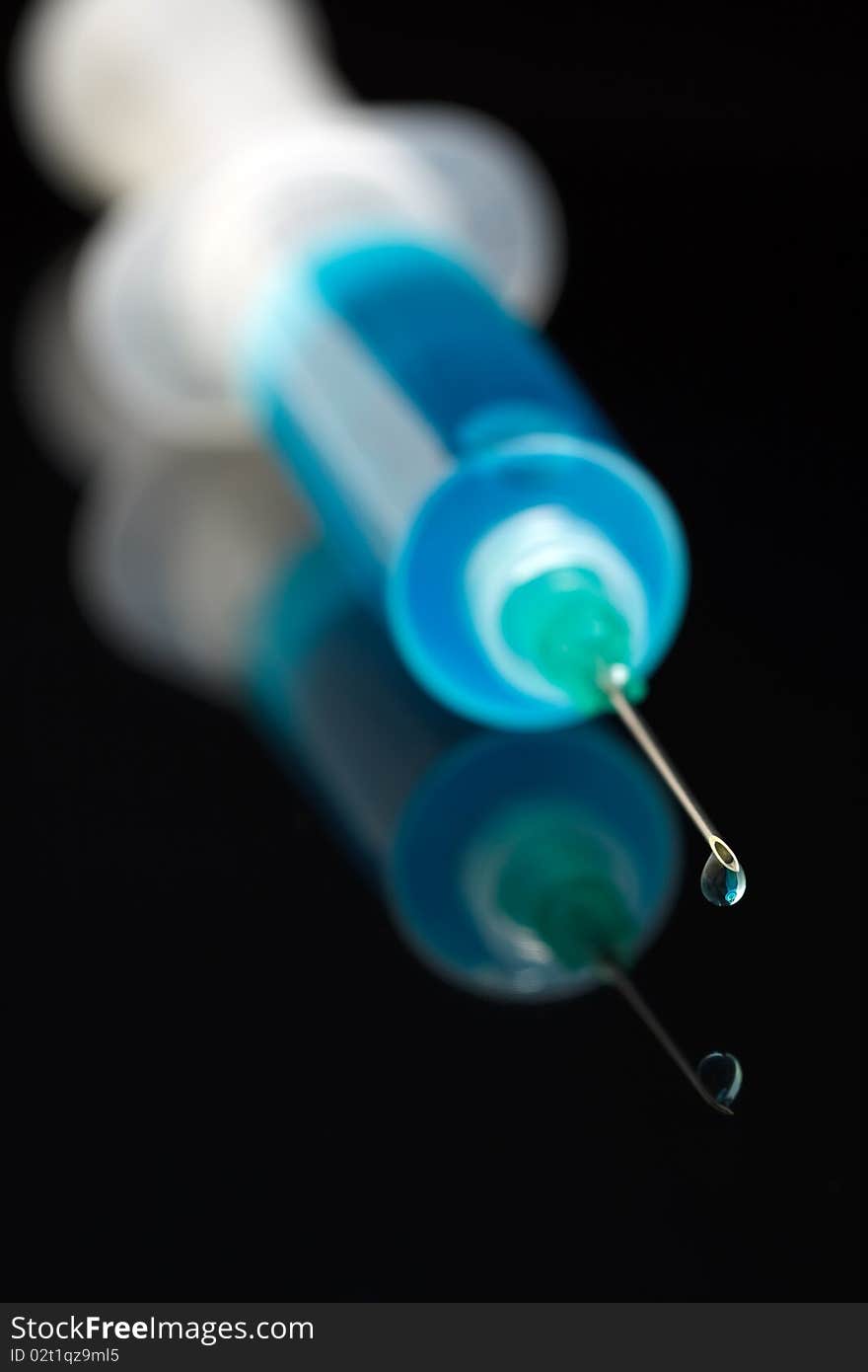 Syringe with blue liquid dripping from the needle on black background. Syringe with blue liquid dripping from the needle on black background