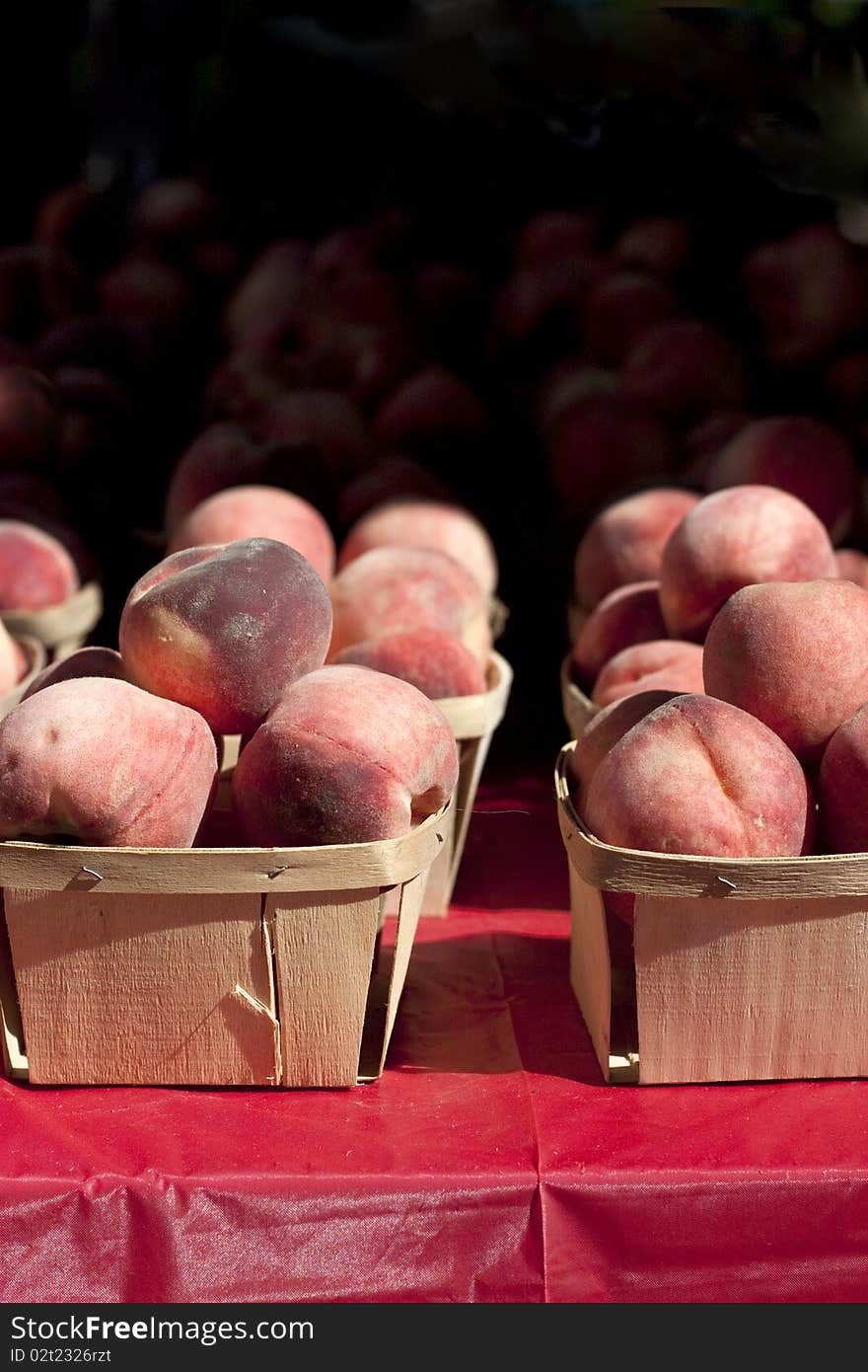 Peaches in a small wooden baskets on a red table cloth.