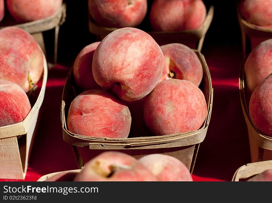 Peaches in a small wooden baskets on a red table cloth.