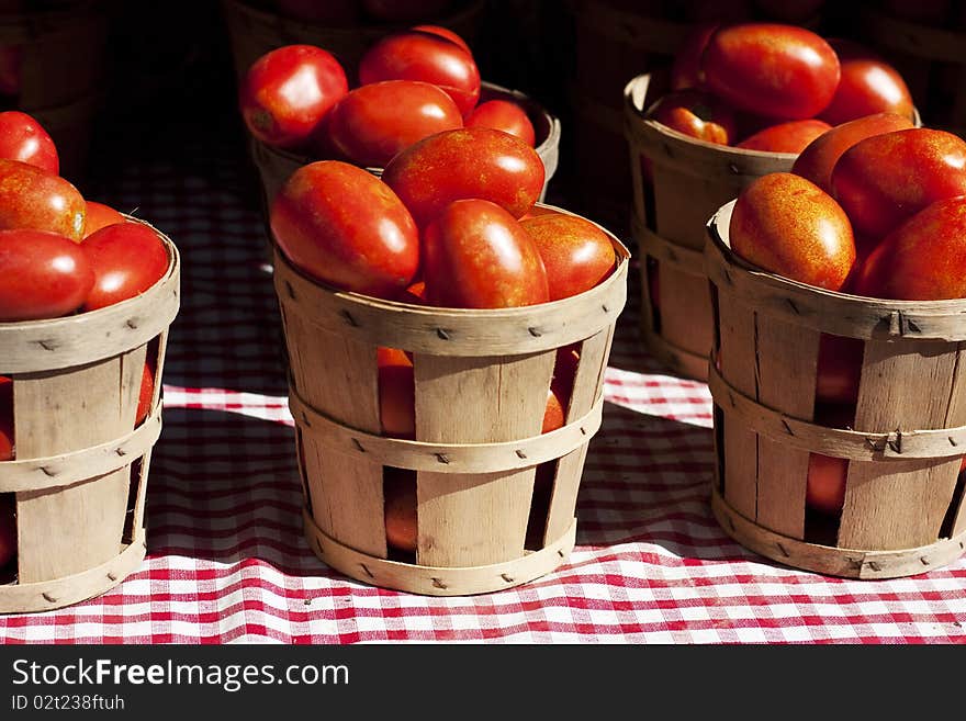 Tomatoes in a small wooden baskets on a red and white table cloth.