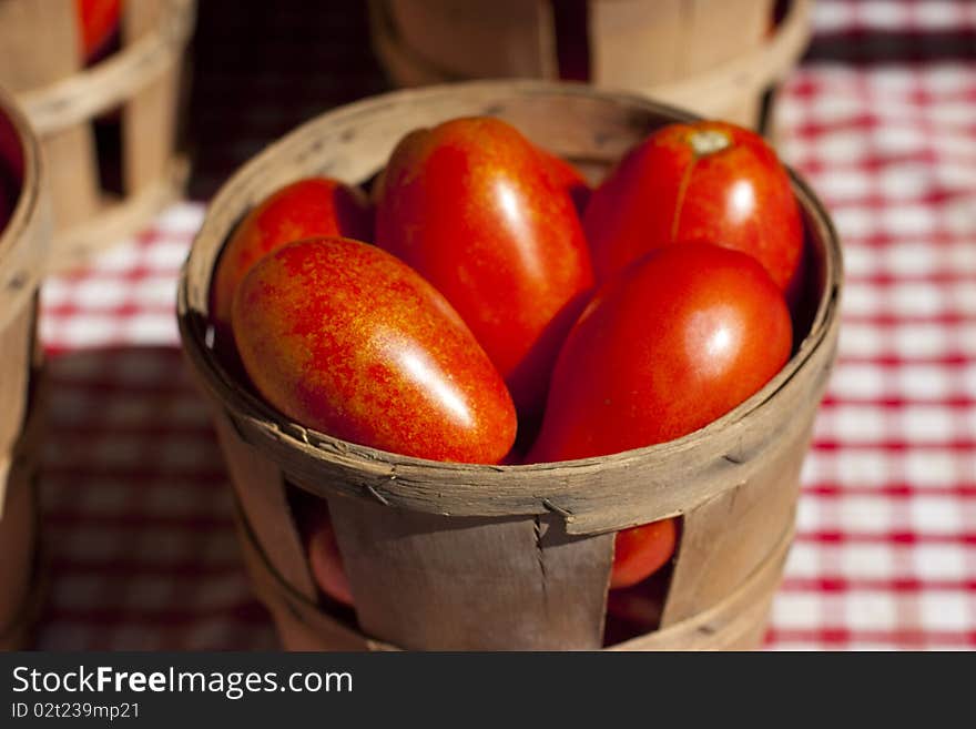 Tomatoes in a small wooden basket on a red and white table cloth.