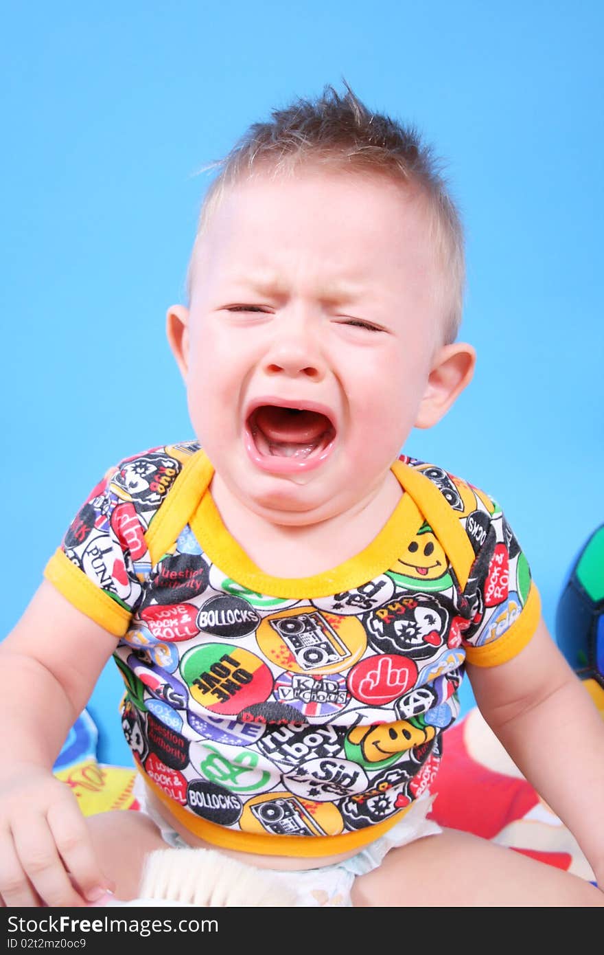 The baby is crying on a blue background. The baby is crying on a blue background