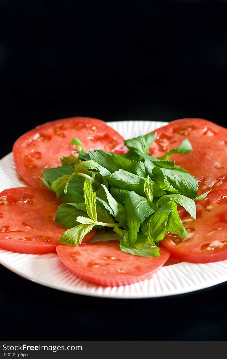 Tomato slices on a white plate isolated on black background