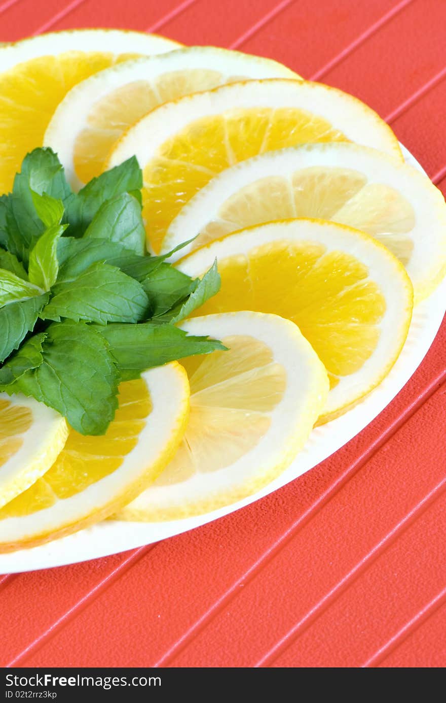 Slices of lemon and orange with mint leaves on red background