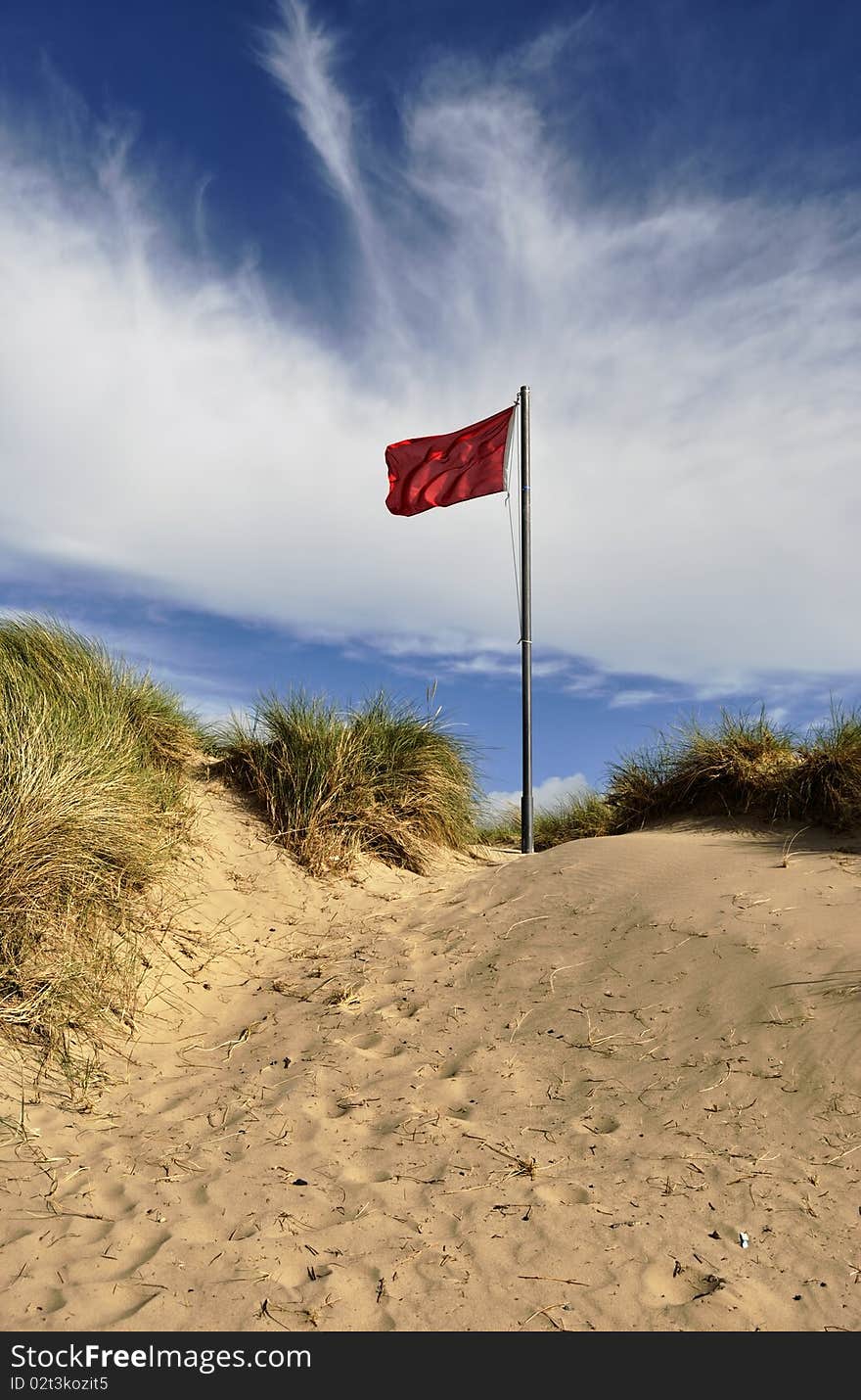 A fluttering red warning flag on a sand dune. A fluttering red warning flag on a sand dune