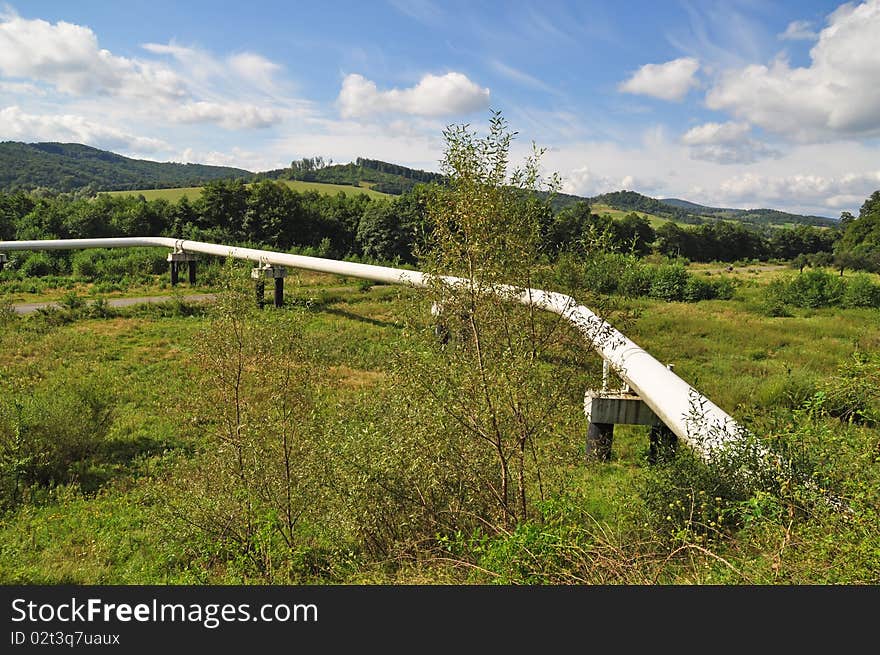 The high pressure pipeline in a summer landscape with the dark blue sky and clouds