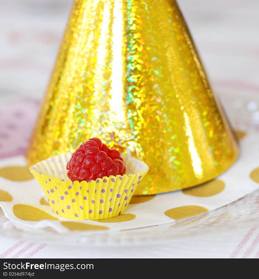 A single raspberry sittung on a plate next to party hat.