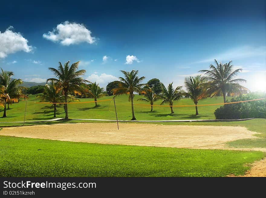 Beautiful tropical vacation resort with blue sky, volleyball court, and palm trees with green grass