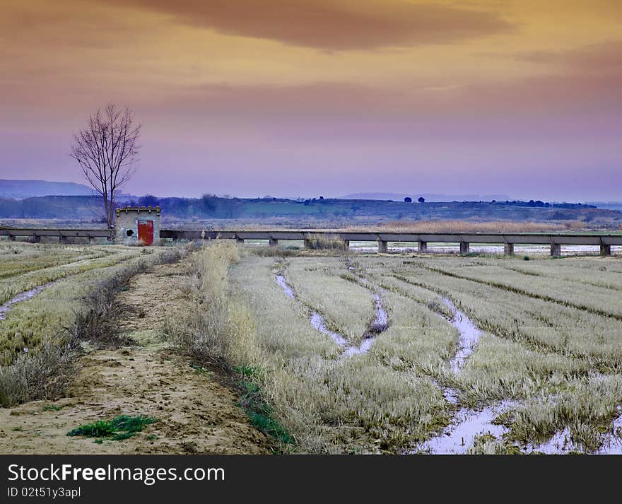 Idilic landscape with little house,water channel and harvest field