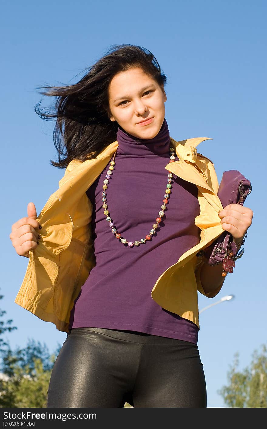 The young smiling woman in a yellow jacket and a bright beads against the blue sky. The young smiling woman in a yellow jacket and a bright beads against the blue sky