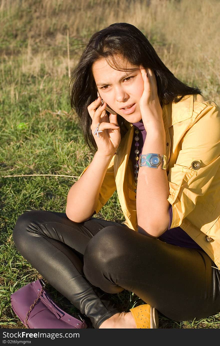 The young woman sits on a lawn and angrily speaks on the phone. The young woman sits on a lawn and angrily speaks on the phone