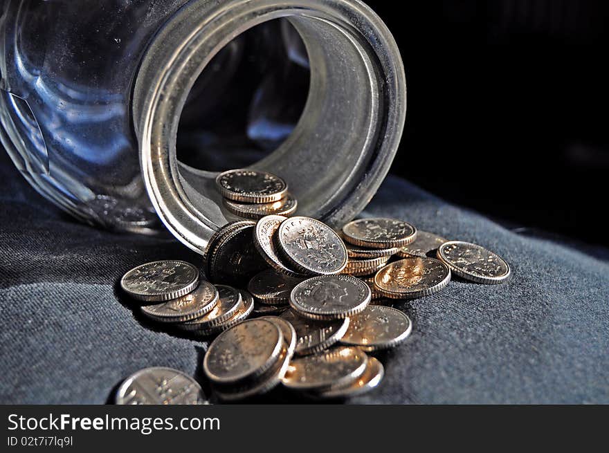 Stash of silver coins spilling from a glass jar against a black and grey background. Stash of silver coins spilling from a glass jar against a black and grey background