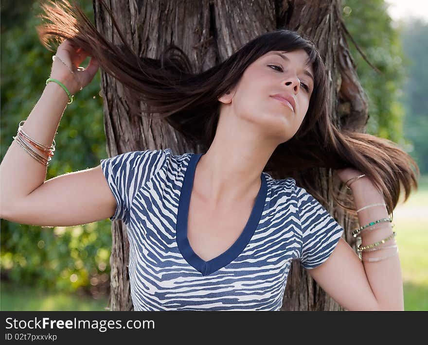 A portrait of a young woman in a blue and white zebra print top, standing outside beside a tree and flinging her hair back. A portrait of a young woman in a blue and white zebra print top, standing outside beside a tree and flinging her hair back.