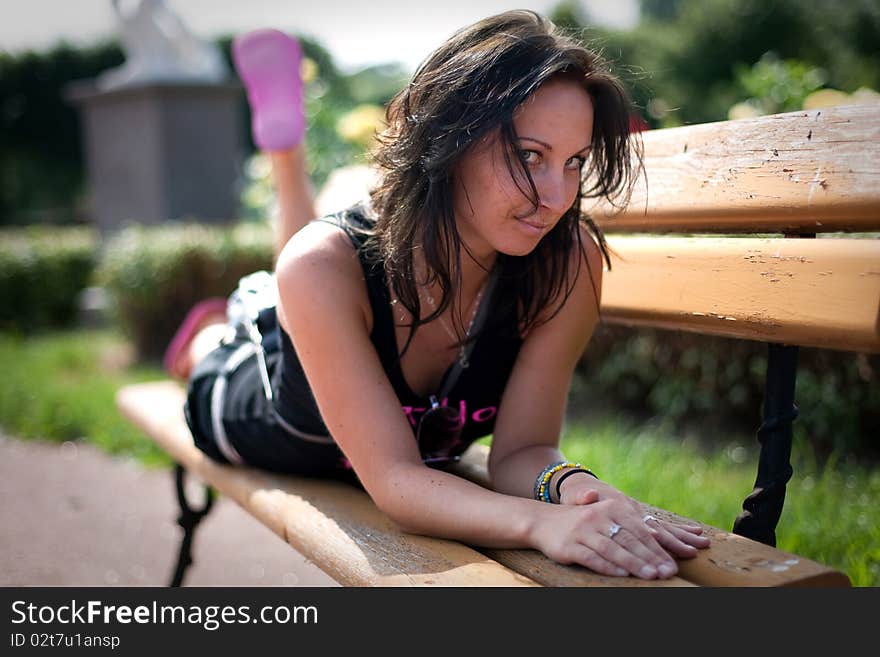 Pretty smiling girl is relaxing on a brench in the park.