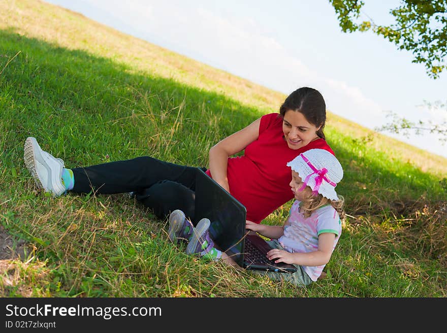 Mother and daughter enjoying summer time outdoors, using a laptop computer. Mother and daughter enjoying summer time outdoors, using a laptop computer