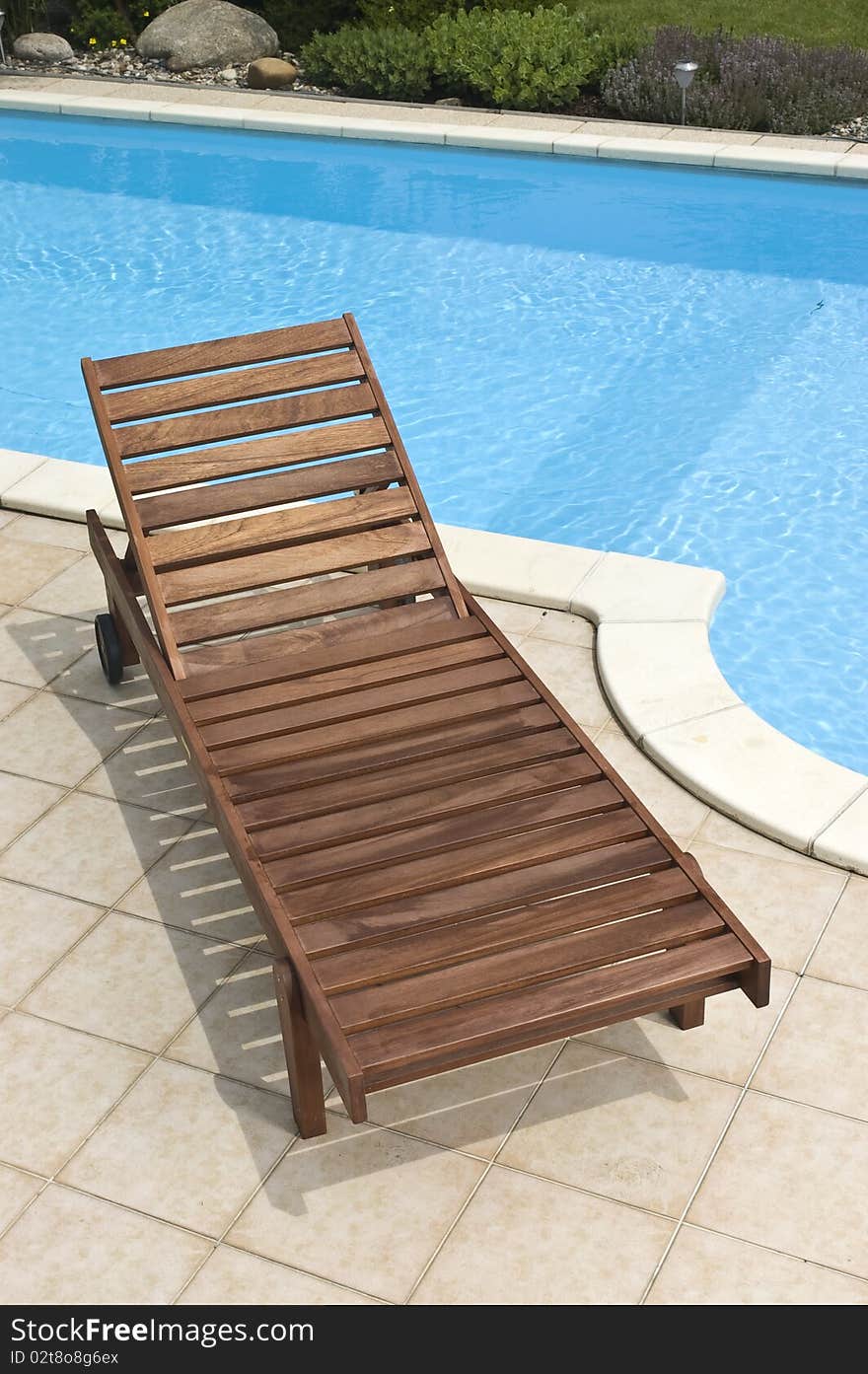 A wooden garden deckchair standing by the pool. A wooden garden deckchair standing by the pool