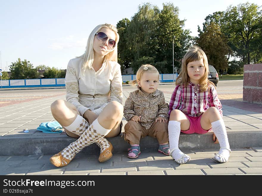 Mum and daughters sit a summer sunny day on a ladder and with enthusiasm look aside. Mum and daughters sit a summer sunny day on a ladder and with enthusiasm look aside