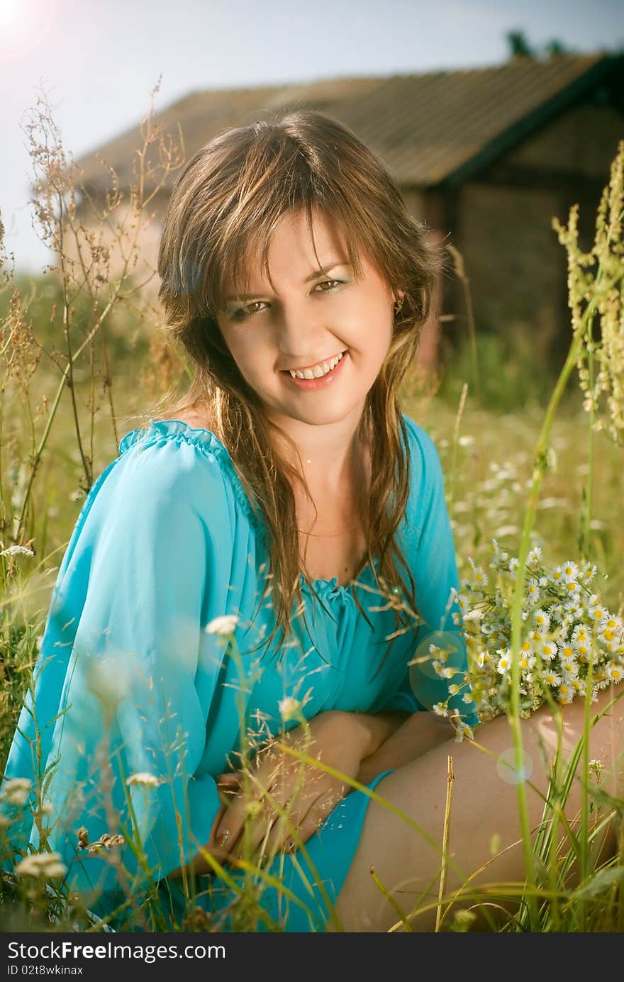 Beautiful girl sitting in a field with a bouquet of flowers