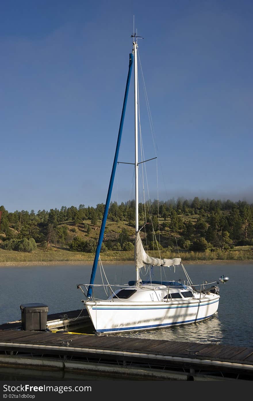 A solitary sailboat sits at the lakeside marina in the early morning light. A solitary sailboat sits at the lakeside marina in the early morning light