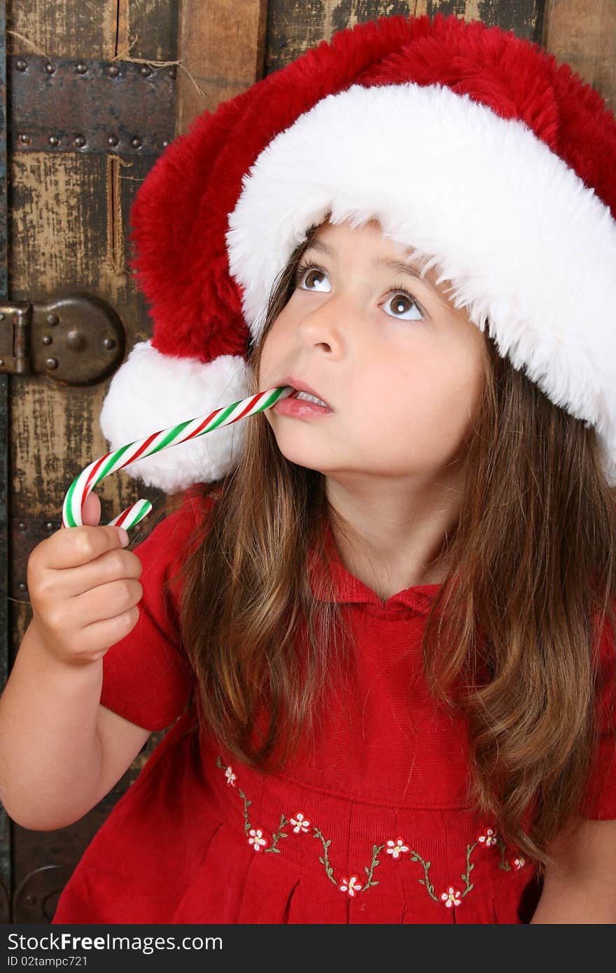 Cute brunette girl wearing a christmas hat, eating candy. Cute brunette girl wearing a christmas hat, eating candy