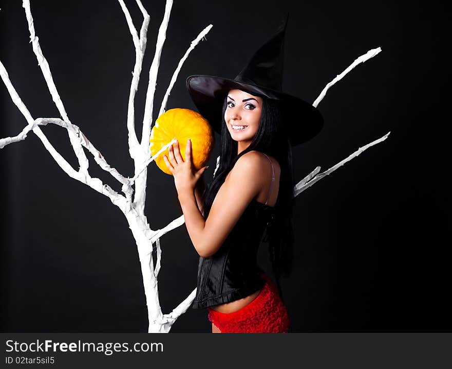 young brunette woman dressed as a witch with a pumpkin