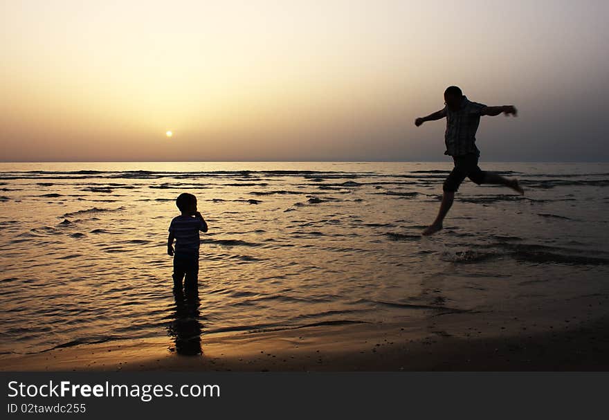 Silhouette image of father and his child by the sea shore, sunset