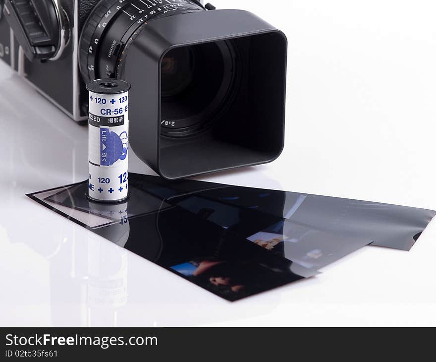 The photo shows a high end camera, a roll film and some slides over white