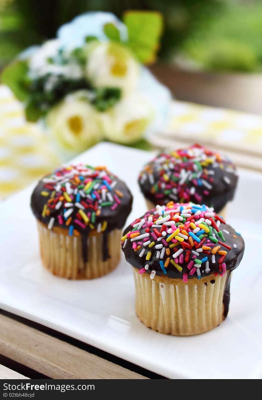 3 muffins on a white plate, placed on a brown table with table decoration and green background. 3 muffins on a white plate, placed on a brown table with table decoration and green background