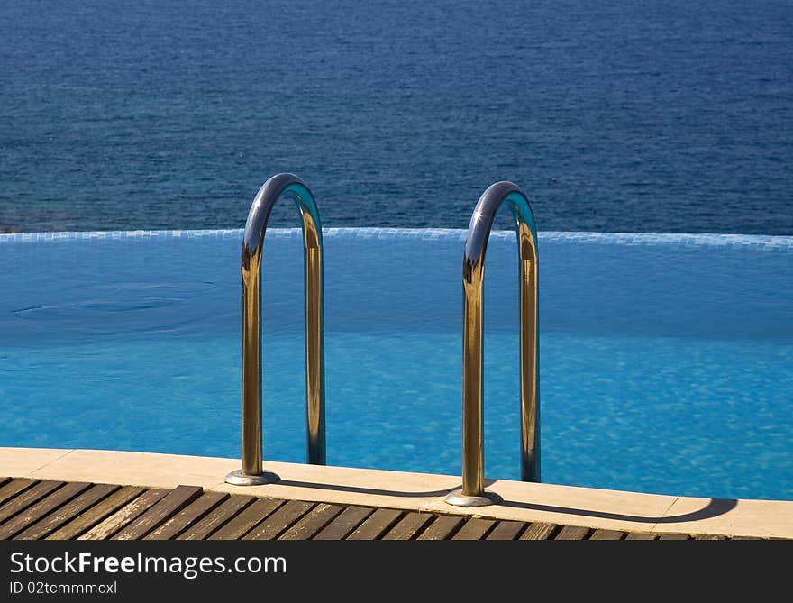 Shot of infinity swimming pool with handrails and blue sea in background. Shot of infinity swimming pool with handrails and blue sea in background