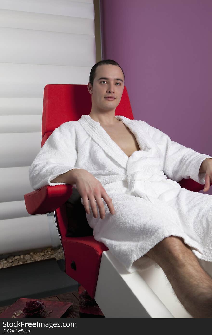 Handsome young man wearing white towel robe, relaxing in pedicure chair. Handsome young man wearing white towel robe, relaxing in pedicure chair