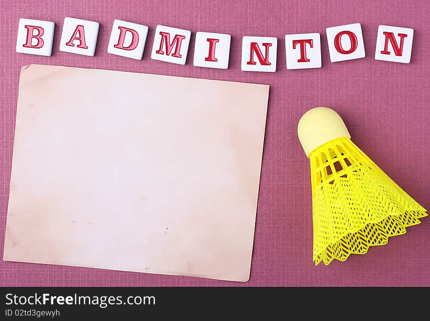 A yellow synthetic badminton shuttlecock next to a piece of paper. Add your text to the paper.