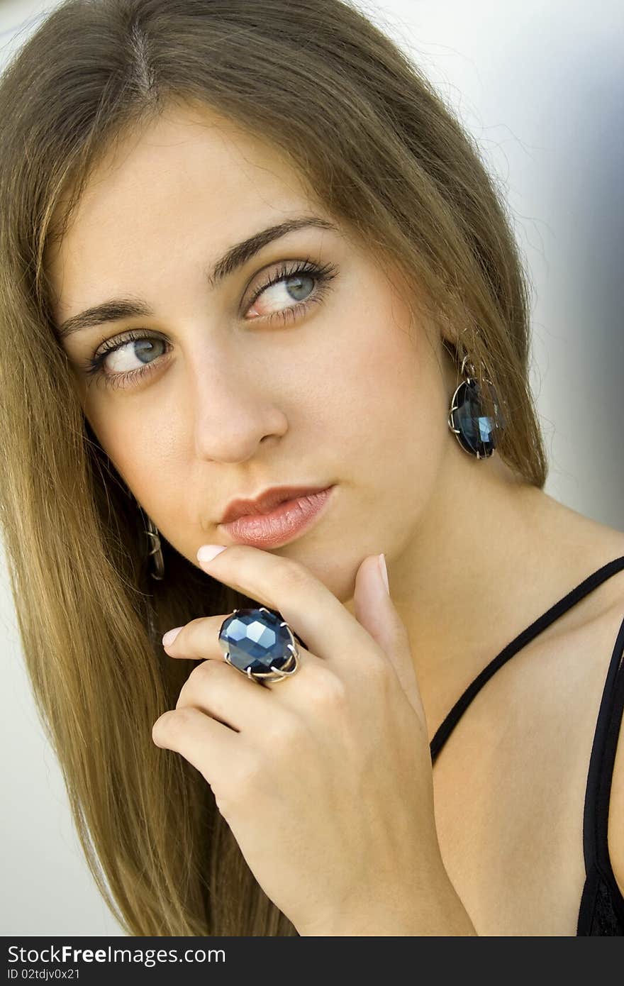 Portrait of elegantly beautiful young woman. The girl beautiful jewelry, ring and earrings with large blue stones. Portrait of elegantly beautiful young woman. The girl beautiful jewelry, ring and earrings with large blue stones