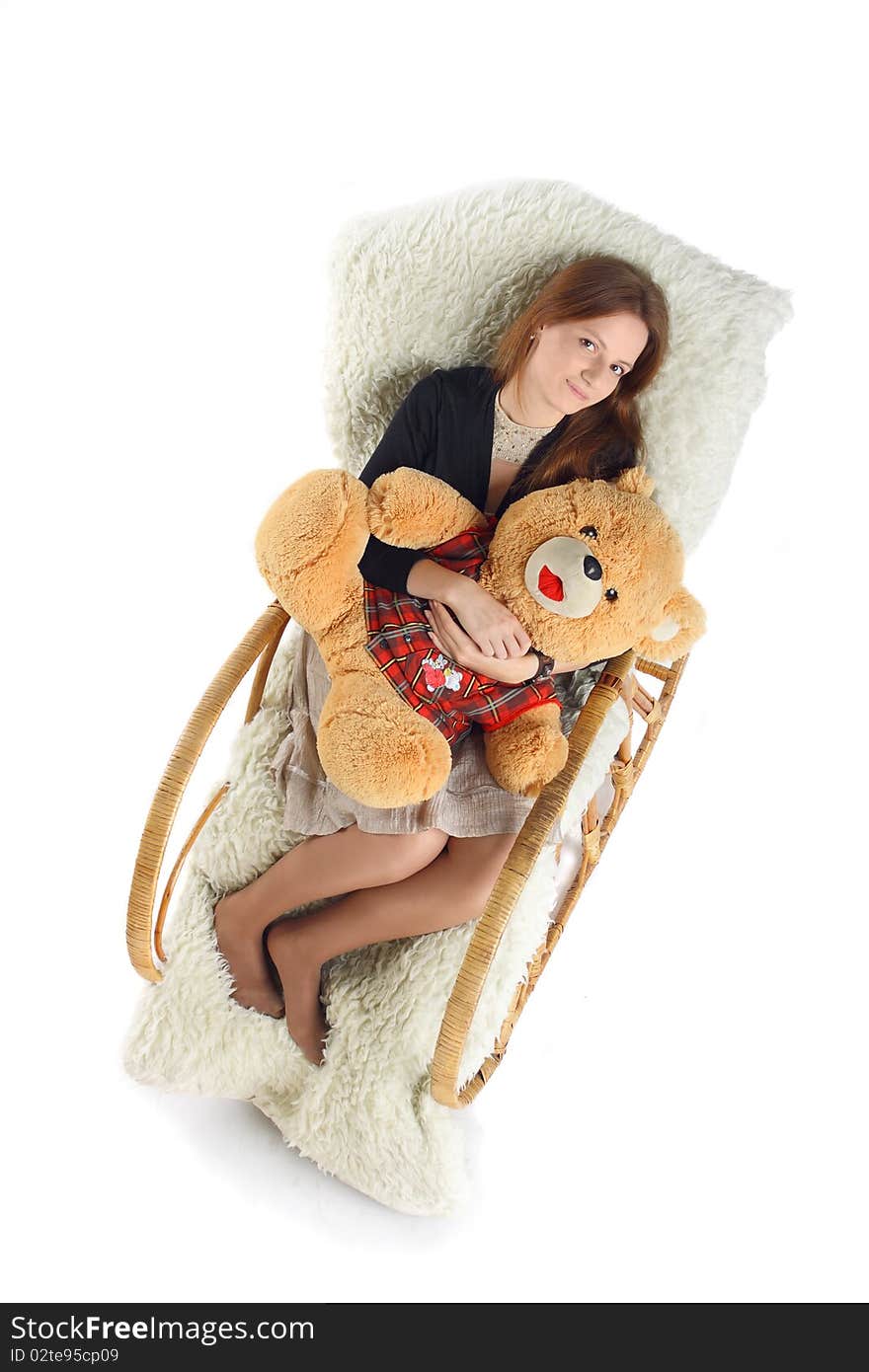 The girl sits in a rocking-chair on white background with a teddy bear in hands