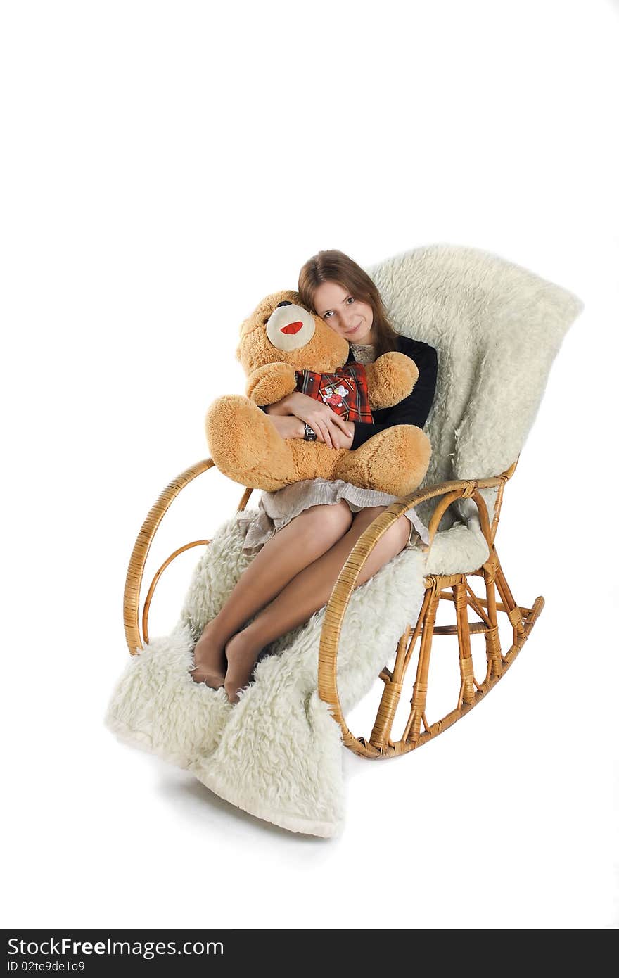 The girl sits in a rocking-chair on white background with a teddy bear in hands. The girl sits in a rocking-chair on white background with a teddy bear in hands