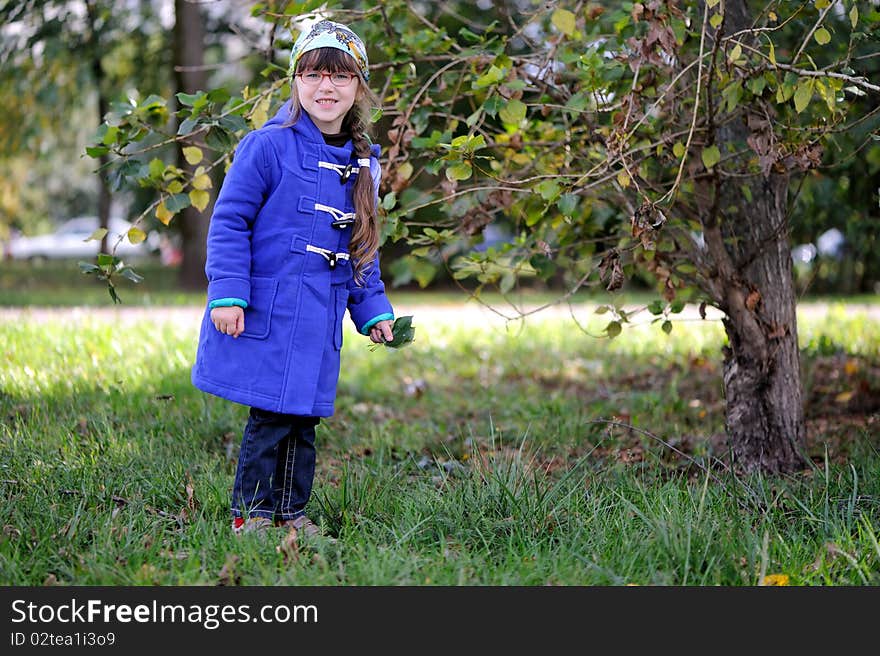 Nice playful little girl in  blue coat and glasses on nice yellow and green background. Nice playful little girl in  blue coat and glasses on nice yellow and green background