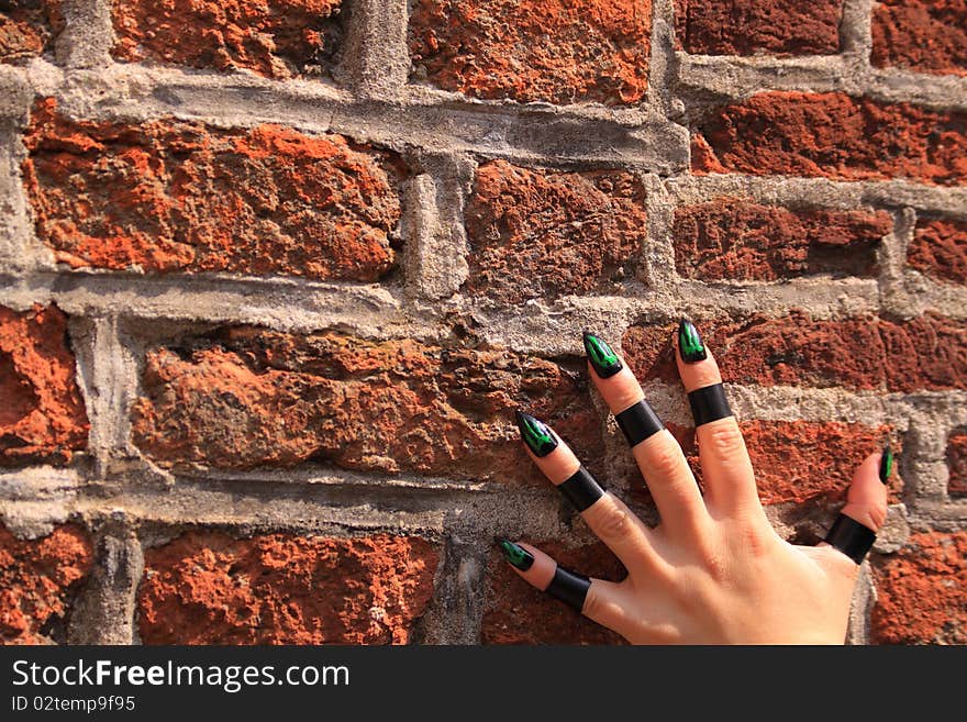 Female hand with green alien nails on a brick wall. Climbing up the wall. Female hand with green alien nails on a brick wall. Climbing up the wall.