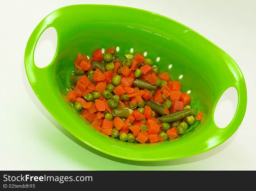 Mixed vegetables in a bright green collander on white background