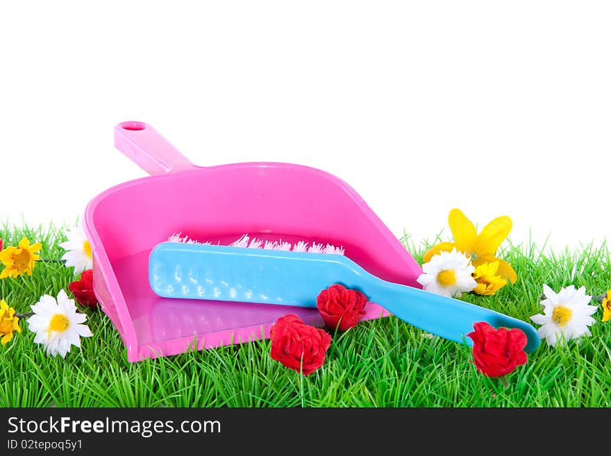 A dustpan and a brush on a flowery green lawn isolated over white