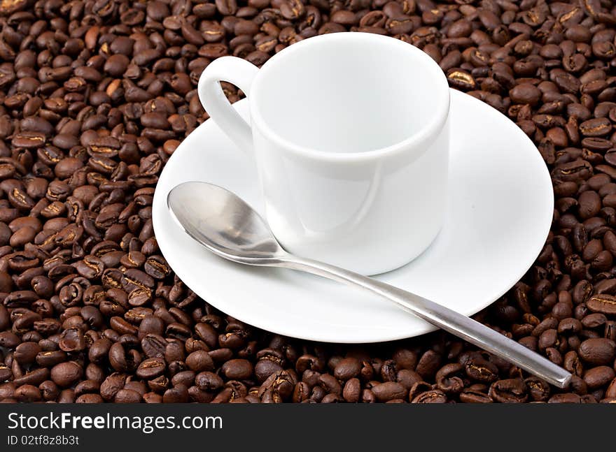 White espresso cup sat on coffee beans with silvered colored spoon