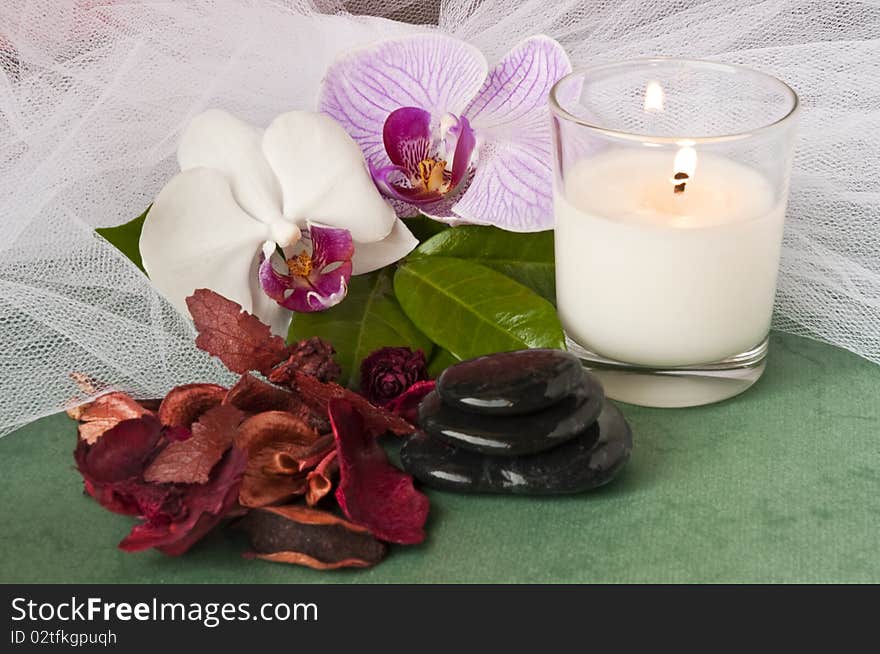 Potpourri  with a lighted candle and orchid on green background. Potpourri  with a lighted candle and orchid on green background