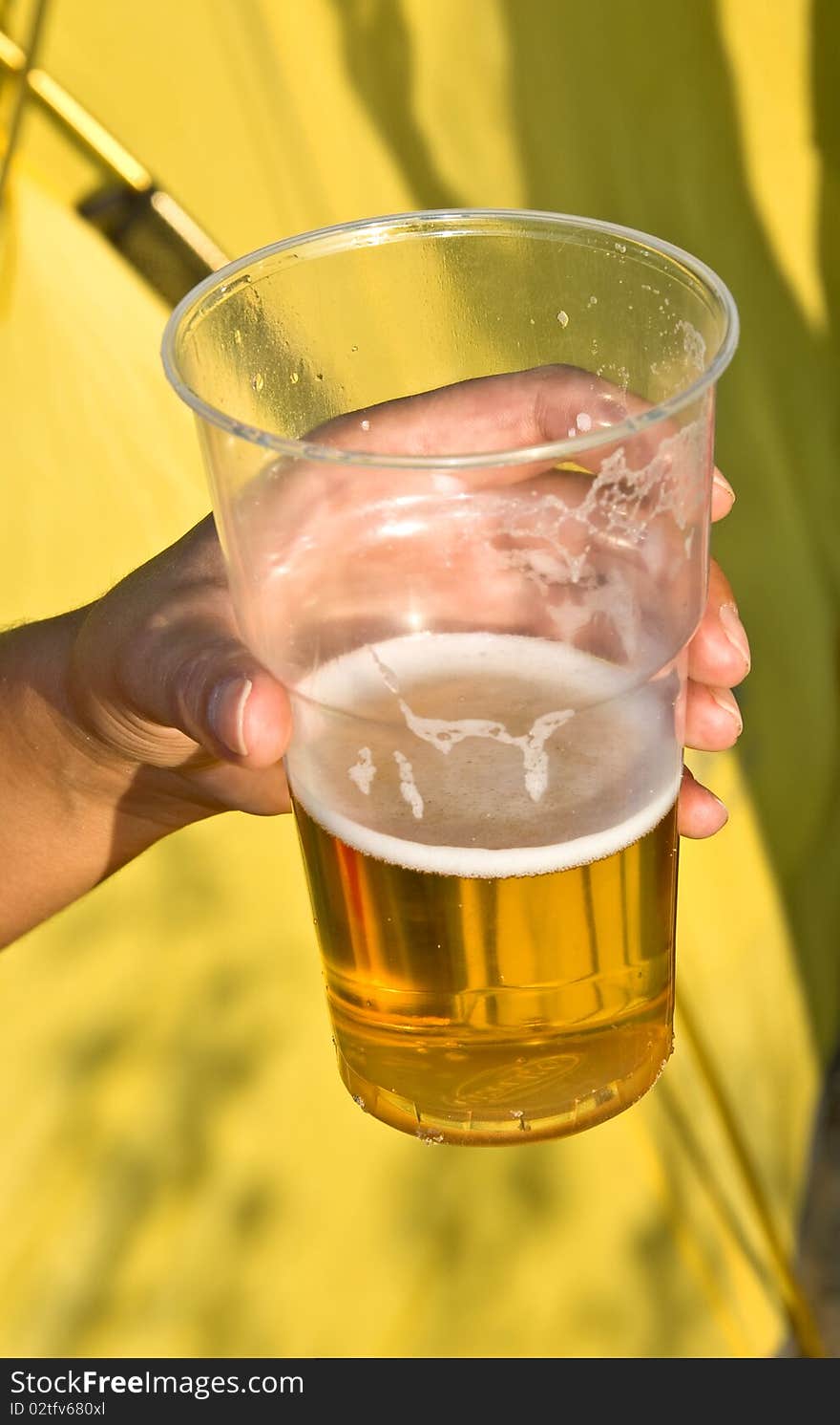 Woman's hand with a glass of beer on a yellow background. Outdoor, summer.