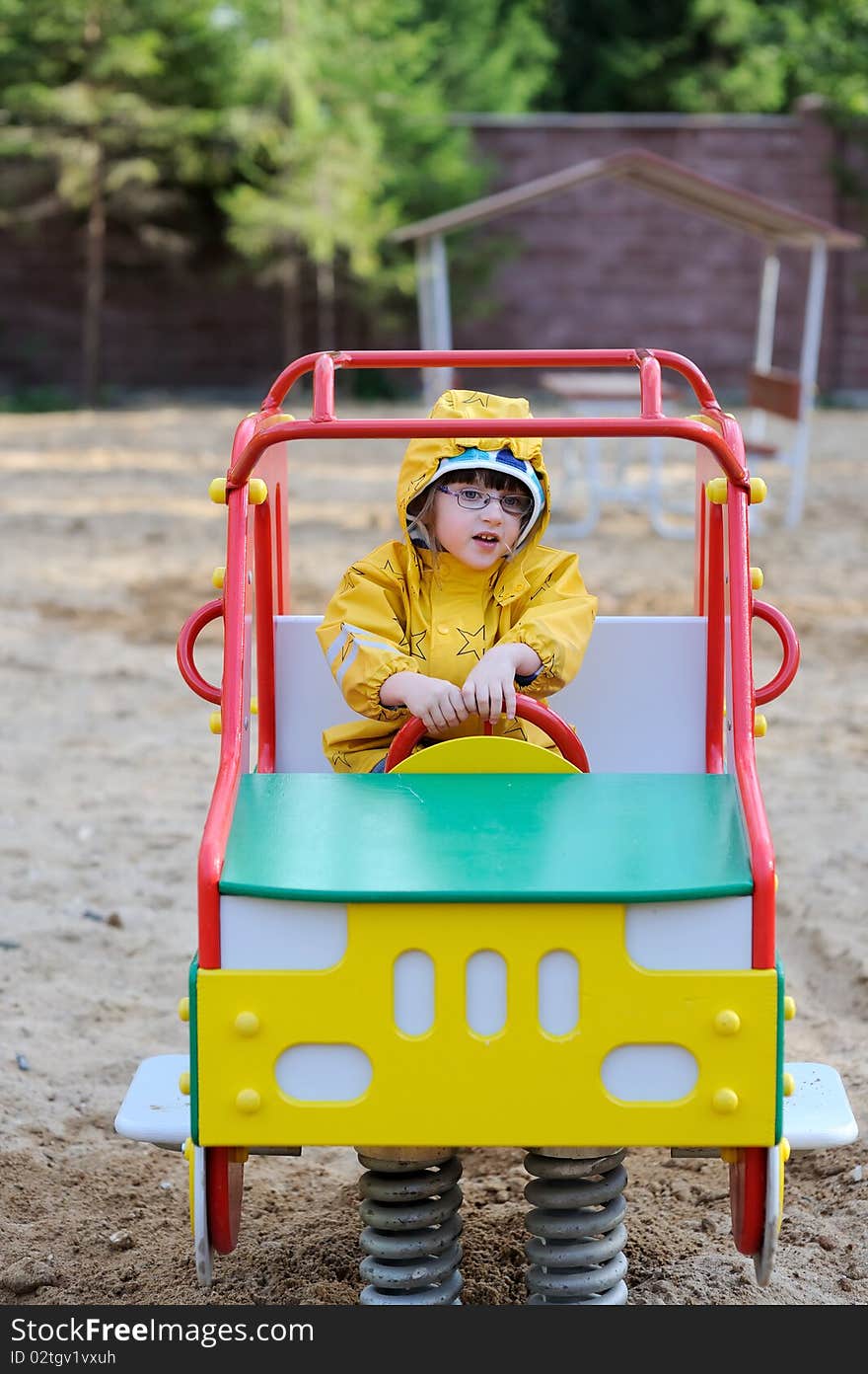 Adorable toddler girl in yellow rain coat playing on playground in playground car. Adorable toddler girl in yellow rain coat playing on playground in playground car