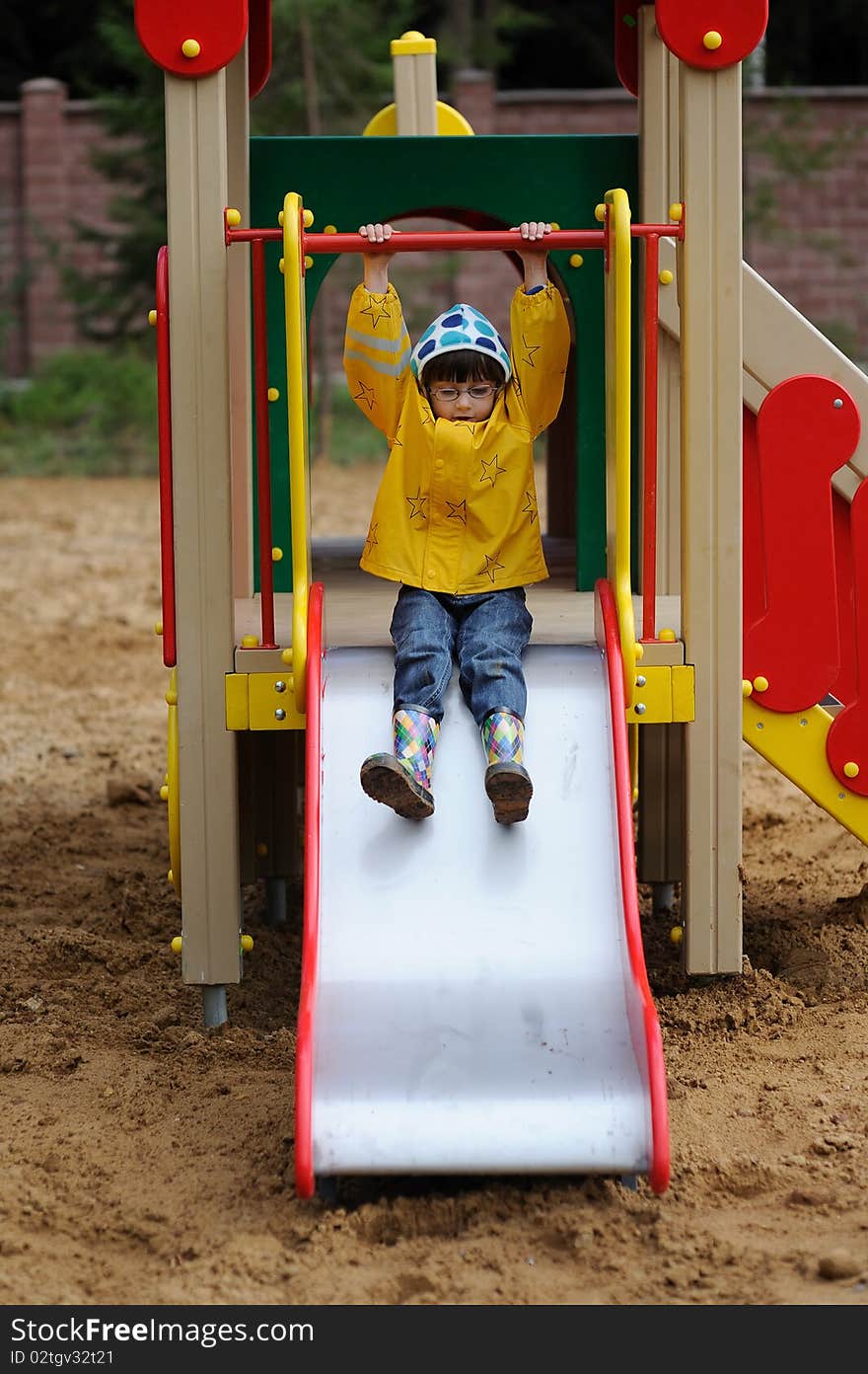 Small girl in yellow rain coat in playground