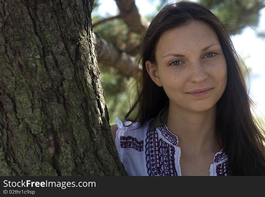 A beautiful young brunette woman stands with an evergreen tree. A beautiful young brunette woman stands with an evergreen tree