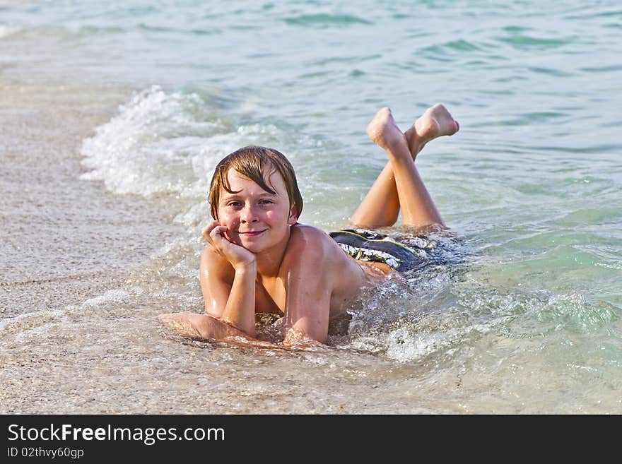 Boy enjoys lying at the beach in the surf