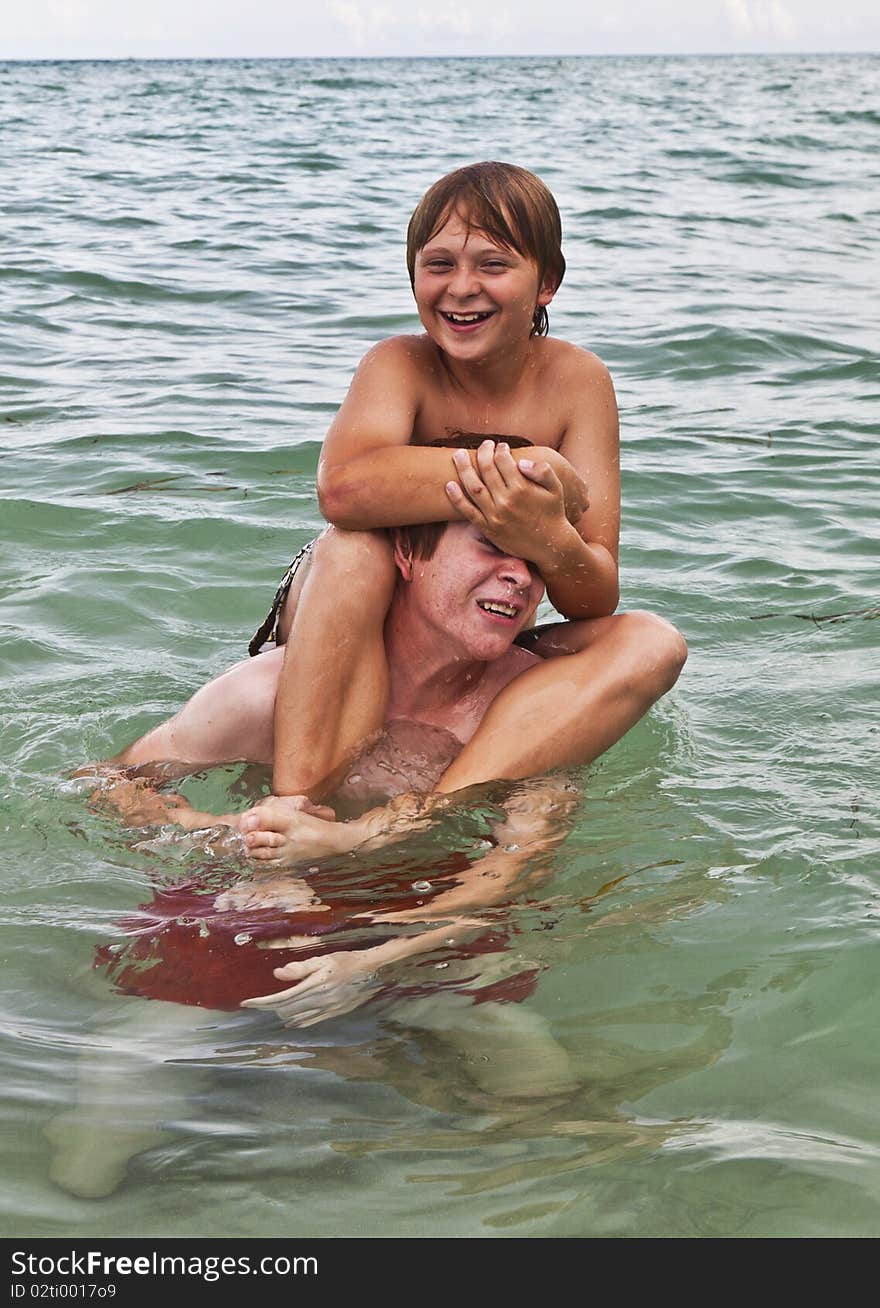 Boys having fun in the beautiful clear sea by playing pickaback