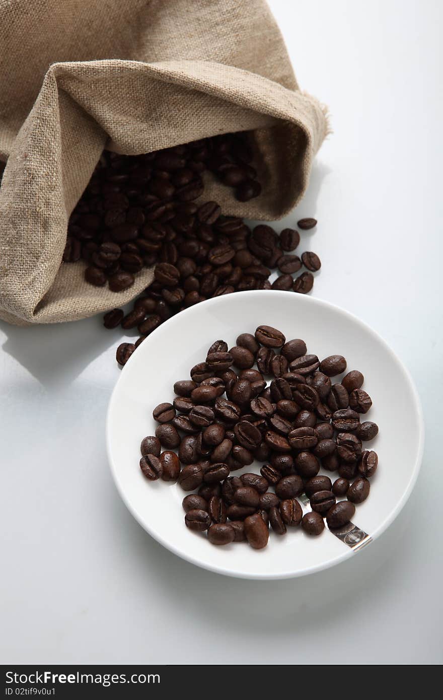 Coffee beans spilled from burlap sack on white background. Coffee beans spilled from burlap sack on white background