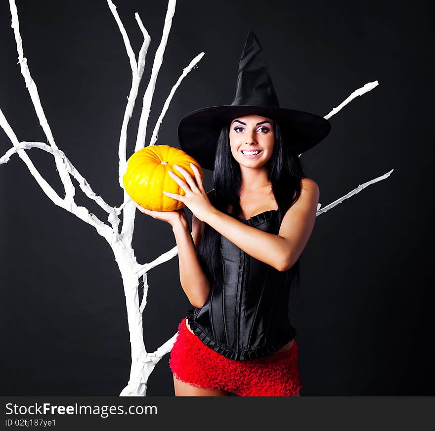 young brunette woman dressed as a witch with a pumpkin