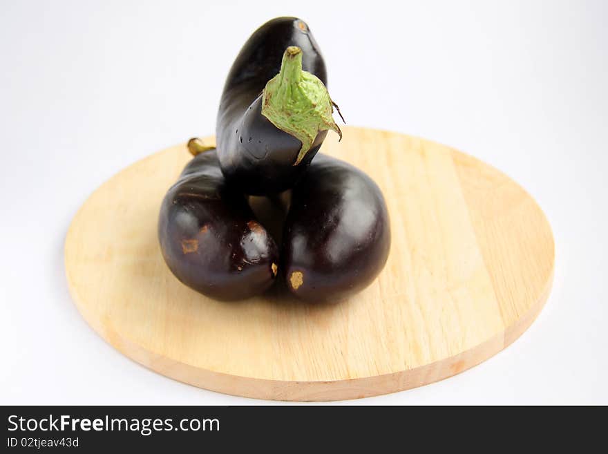 Three purple eggplant on a wooden board on a white background