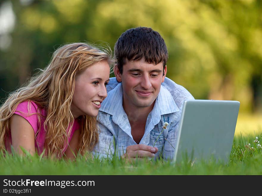 A couple relaxing in the park with a laptop, lying on the grass